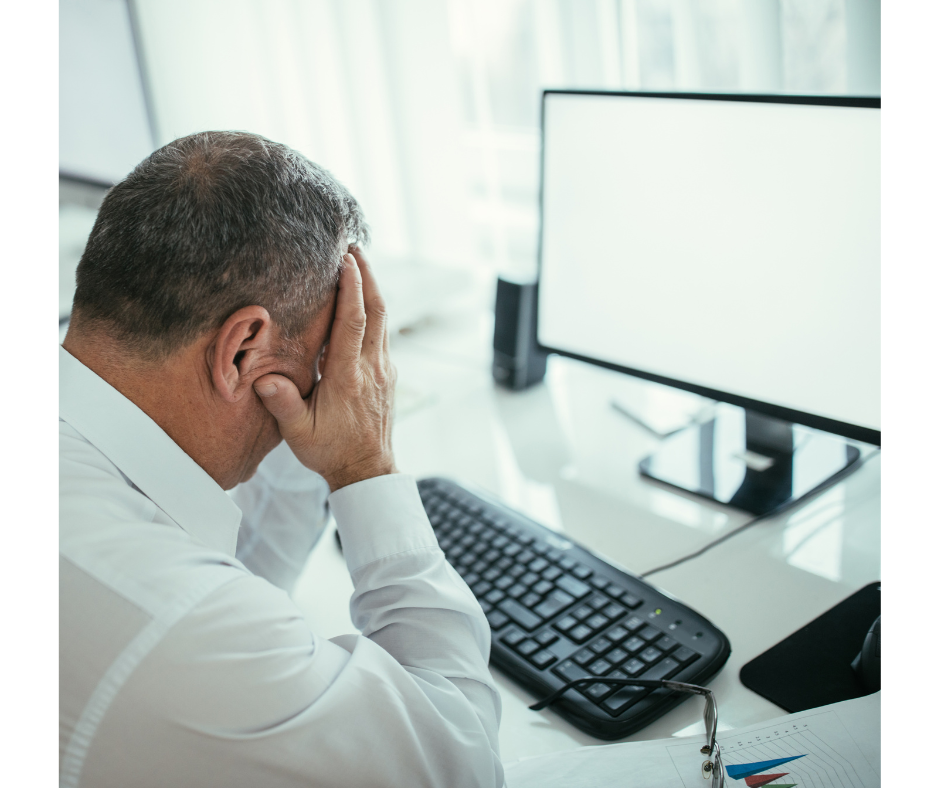 Frustrated businessman, head down with both hands on face, looking at blank computer screen